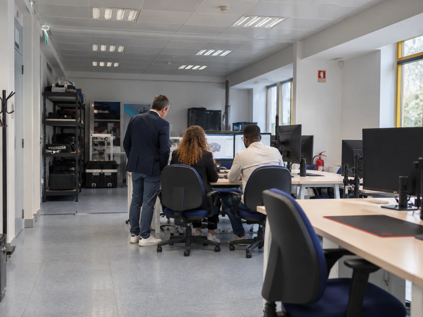 Equipo visto de espaldas colaborando en una mesa compartida con ordenadores y notas de proyecto