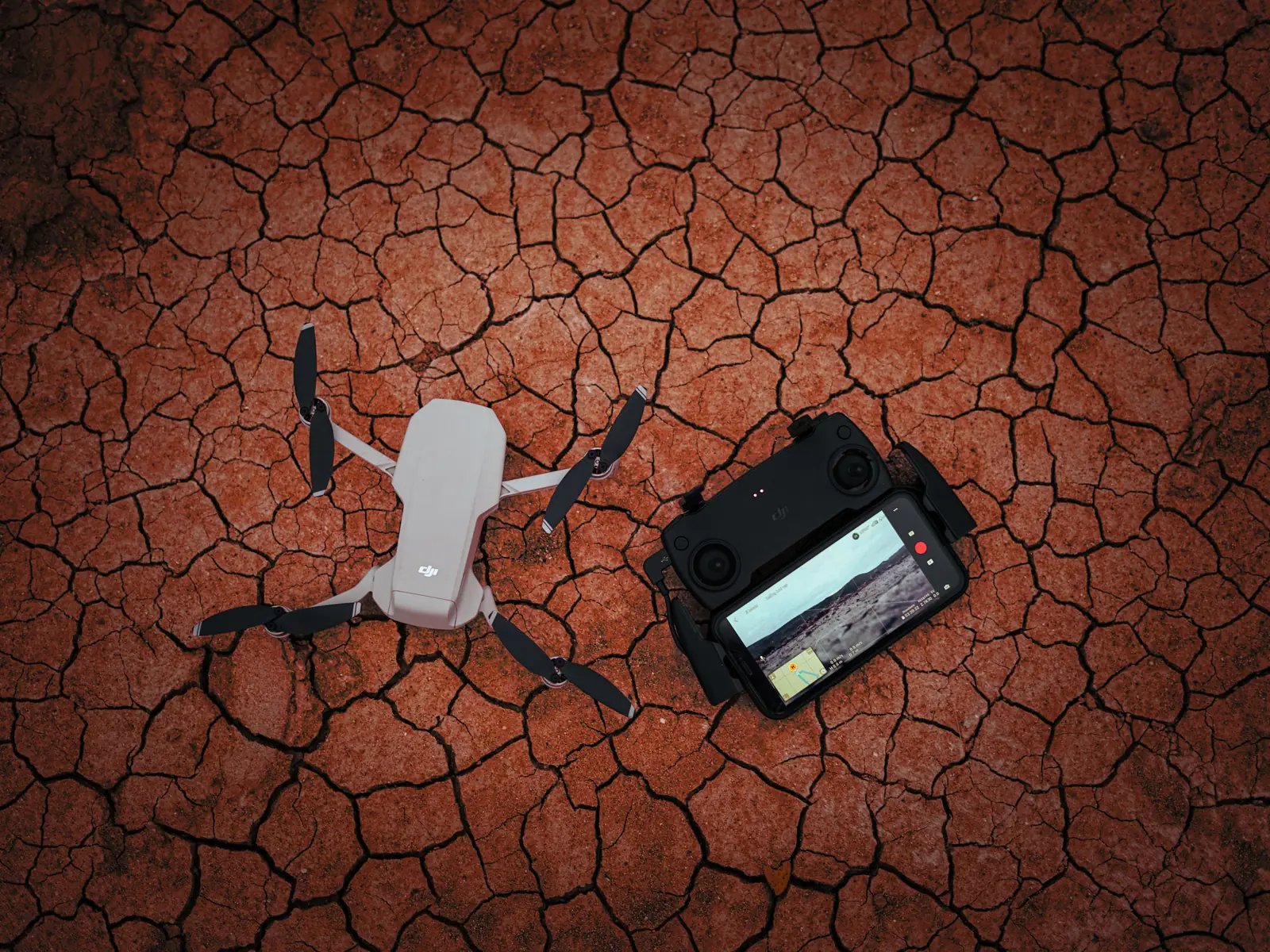 Drone e comando pousados no terreno, prontos para o levantamento.